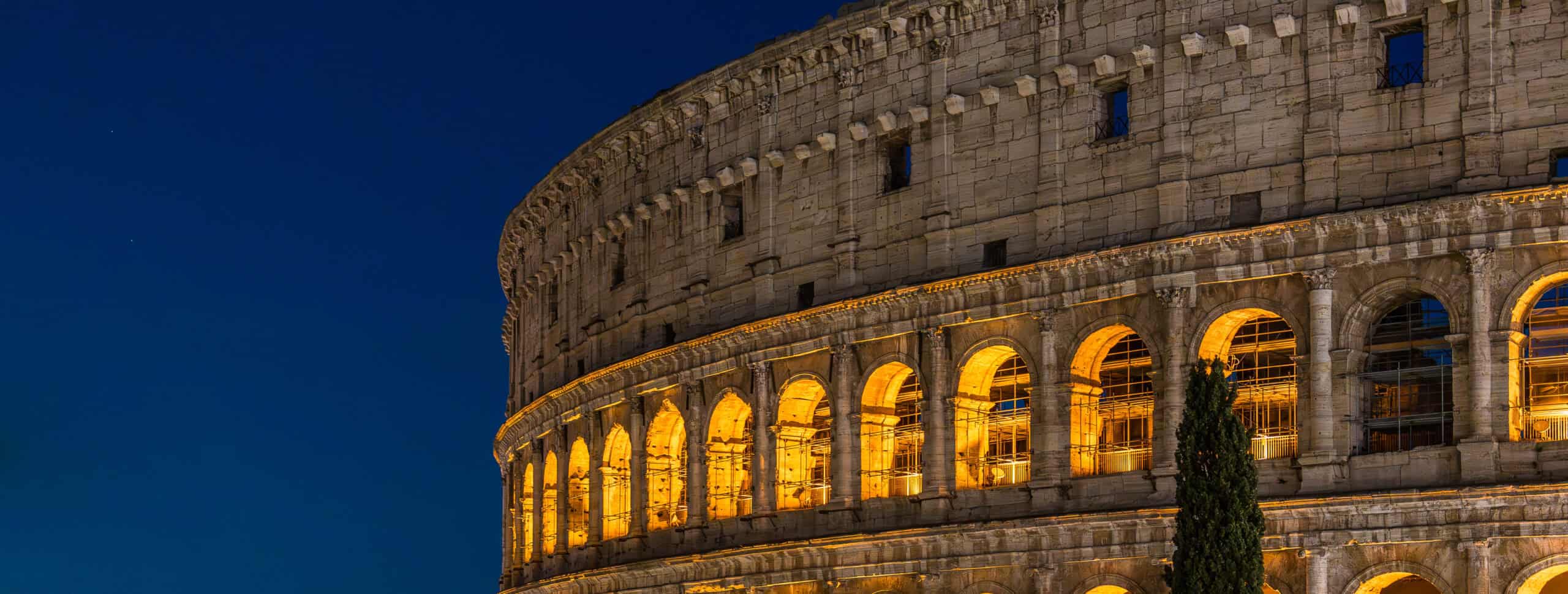 Illuminated arches of the Colosseum in Rome at night with deep blue sky backdrop