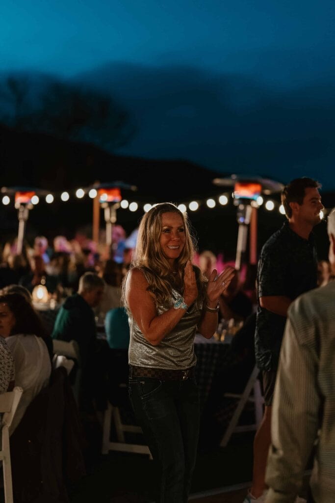 Female guest clapping and smiling at night event with bistro lighting and seated dinner crowd