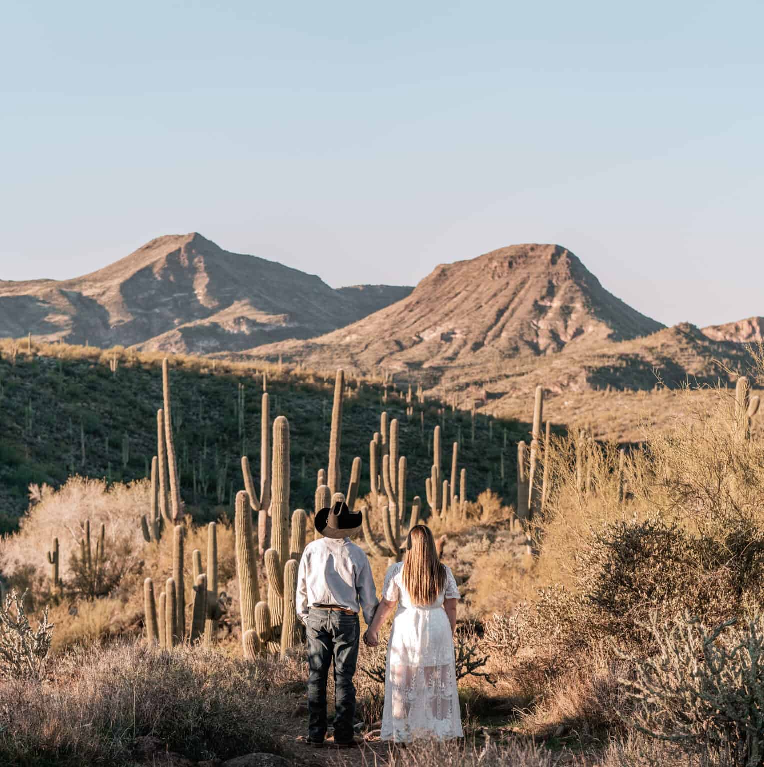bride and groom holding hands in Phoenix desert engagement session with saguaro cacti