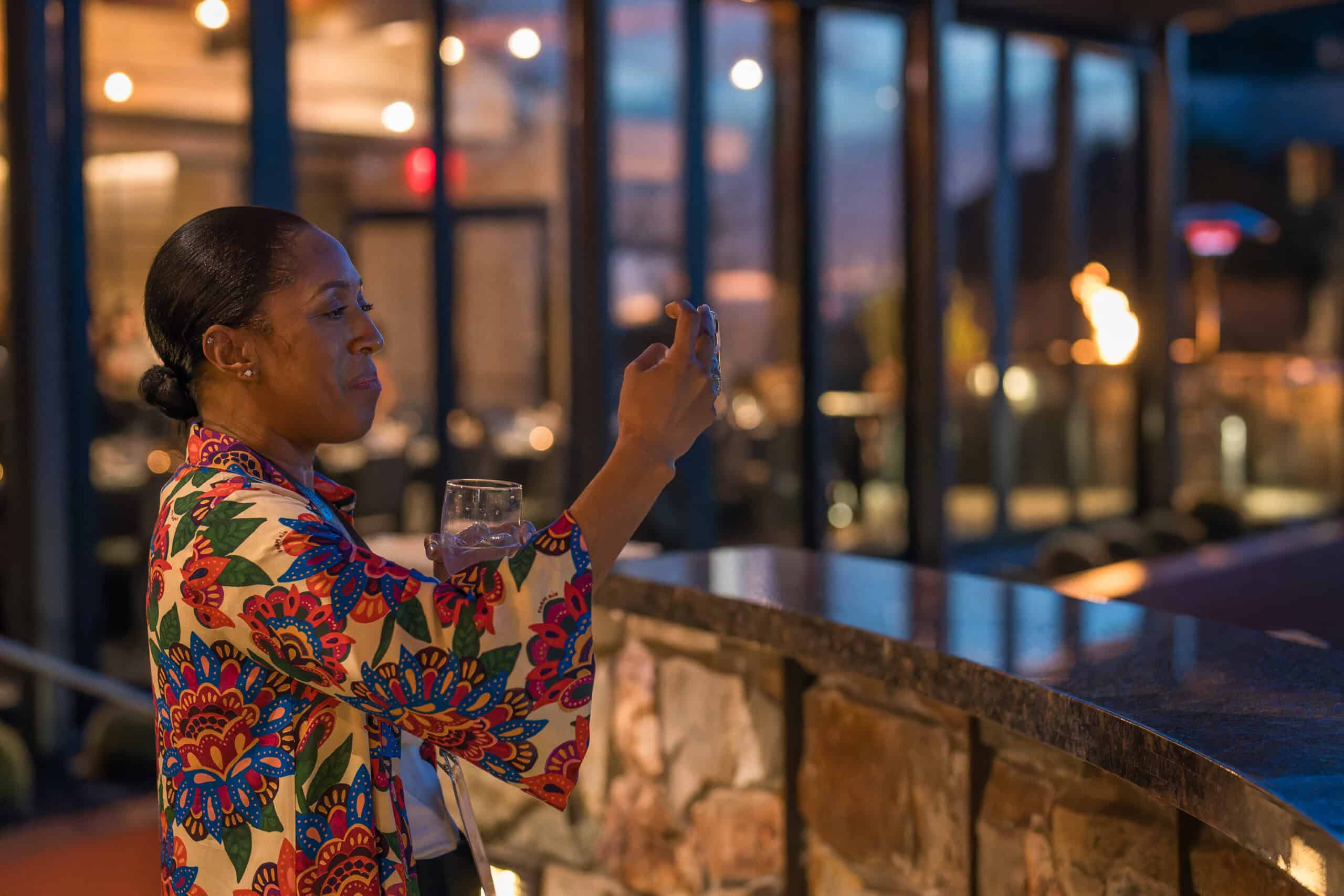 Woman enjoying cocktail hour while recording moments on her phone during a Virginia Beach evening event.