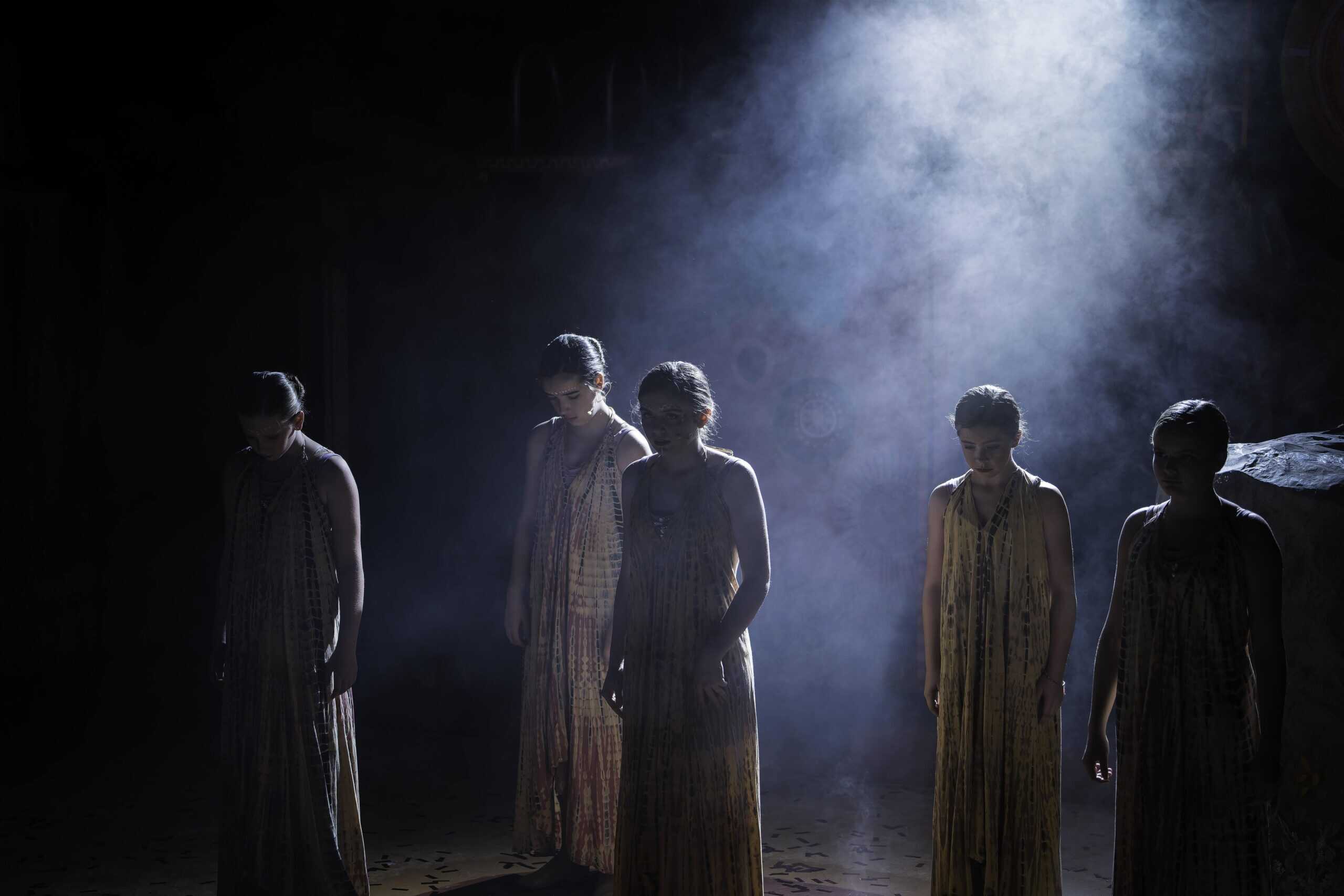 Dance troupe in flowing costumes standing in fog-lit stage atmosphere during performance