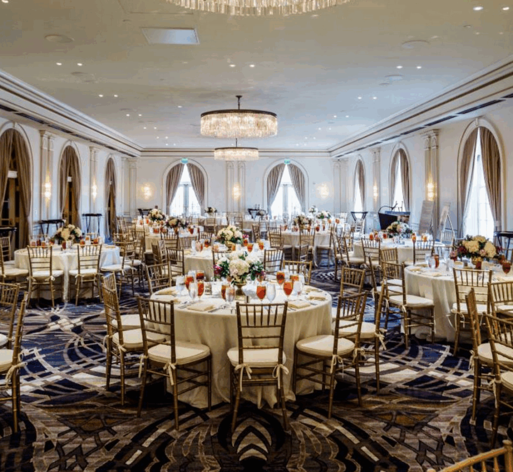 A glamorous wedding reception in the Crystal Ballroom at The Cavalier Hotel, featuring sparkling chandeliers, round tables with floral centerpieces, captured by a Virginia Beach wedding photographer.