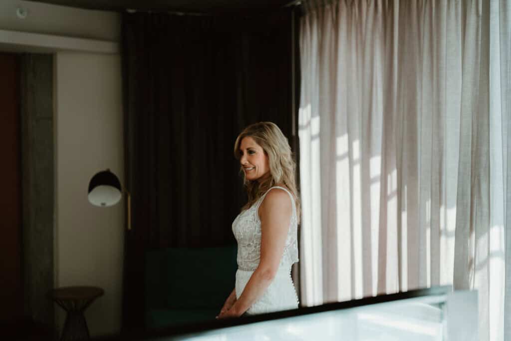 Bride standing by a window in soft natural light, captured during wedding preparation in Hampton Roads