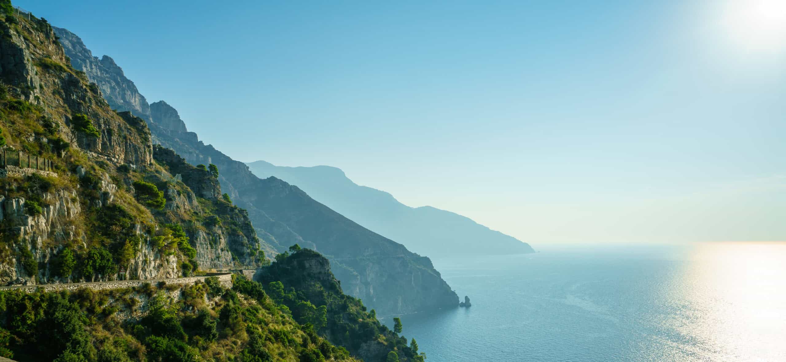 Panoramic view of the Amalfi Coast cliffs in Italy with sunlit Mediterranean Sea and winding coastal road