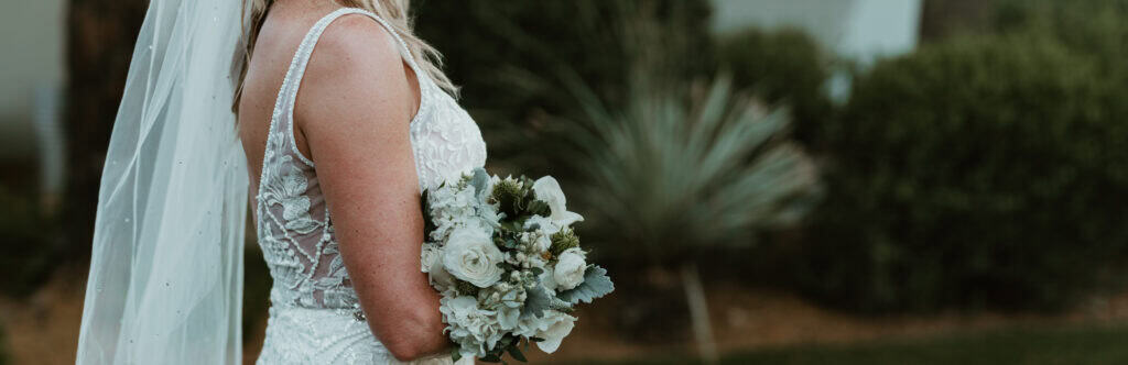 Bride in Virginia Beach wedding gown holding white rose and hydrangea bouquet outdoors. Taken by a Virginia Beach Photographer.