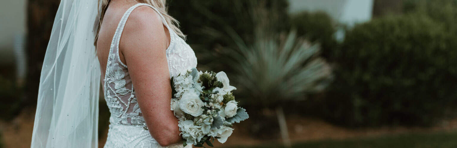 Bride in Virginia Beach wedding gown holding white rose and hydrangea bouquet outdoors