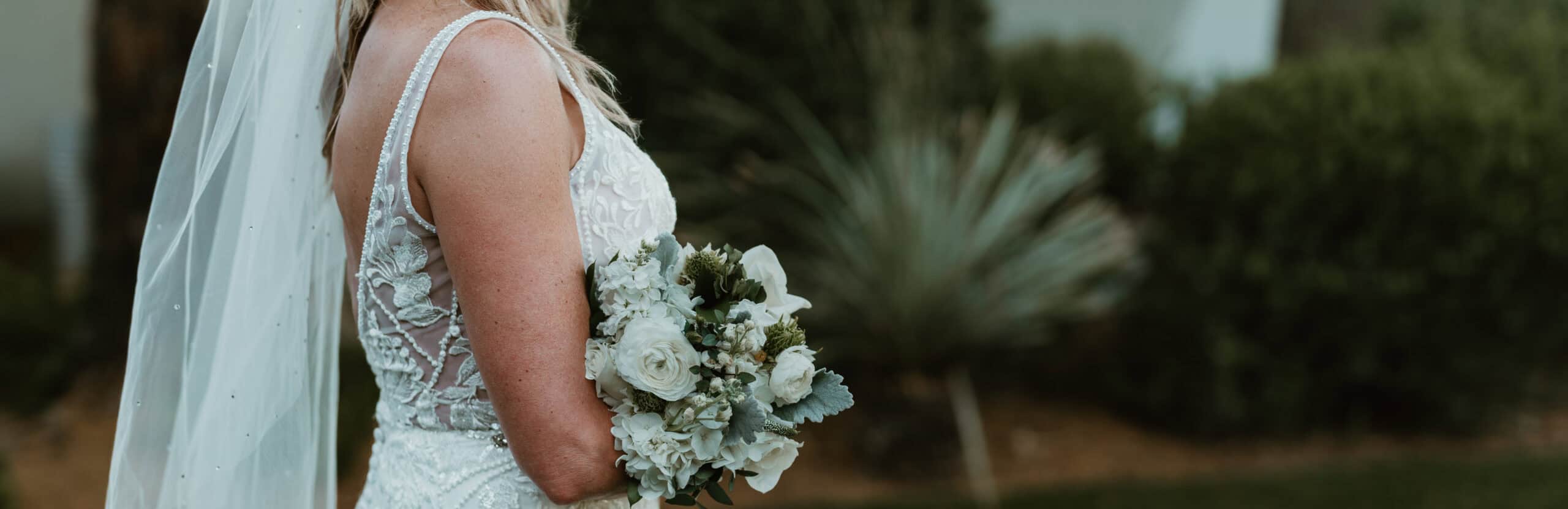 Bride in Virginia Beach wedding gown holding white rose and hydrangea bouquet outdoors