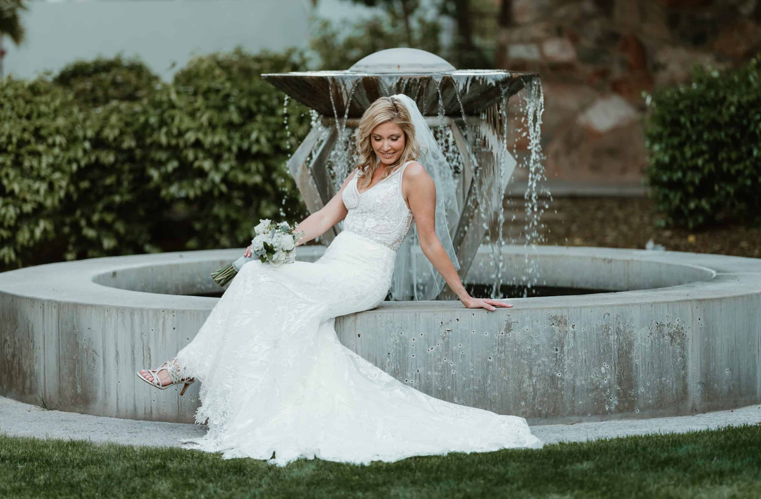 Bride in lace gown posing by a fountain during golden hour in Virginia Beach, captured by wedding photographer Captured in VA