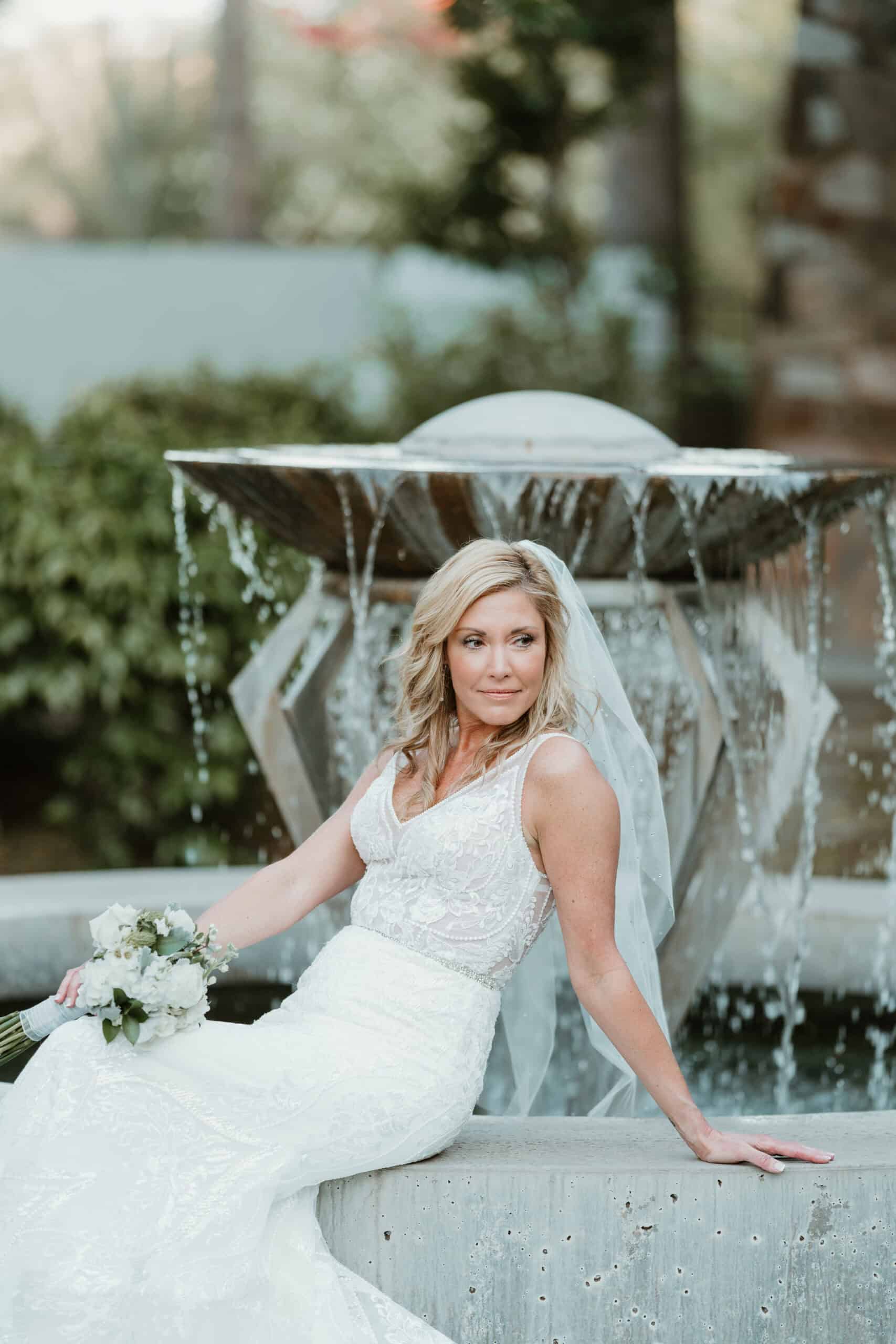 Portrait of bride seated by fountain in Virginia Beach wedding gown holding bouquet