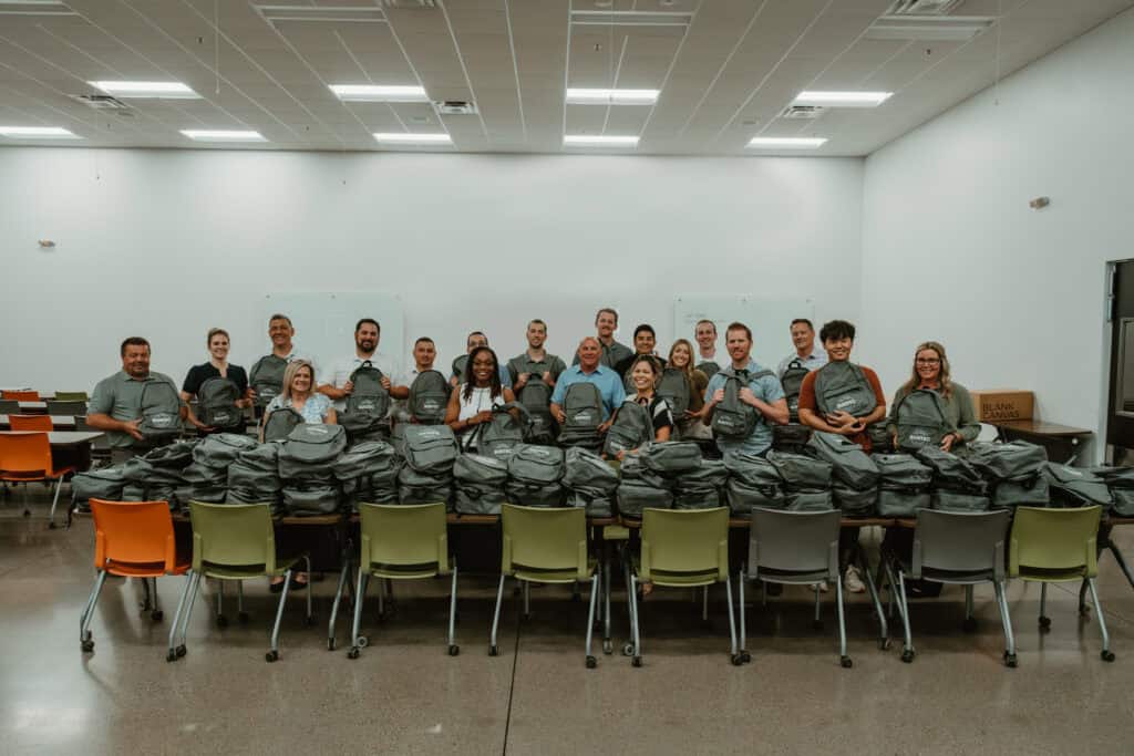 Volunteers posing behind tables filled with packed backpacks for community outreach in Virginia Beach