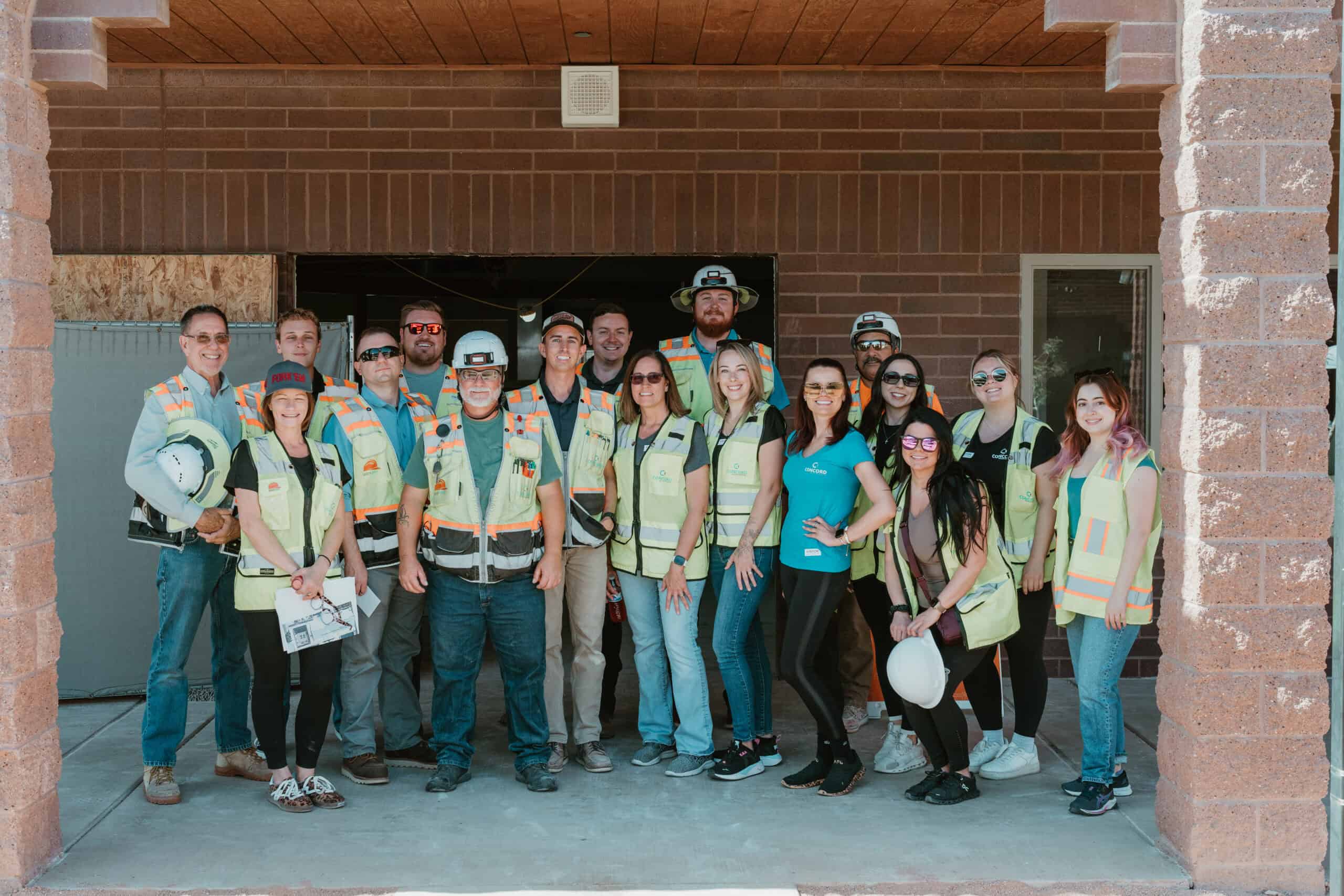 A diverse group of construction professionals in hard hats and high-visibility vests stands in front of a building, likely at a Virginia Beach construction event or job site.