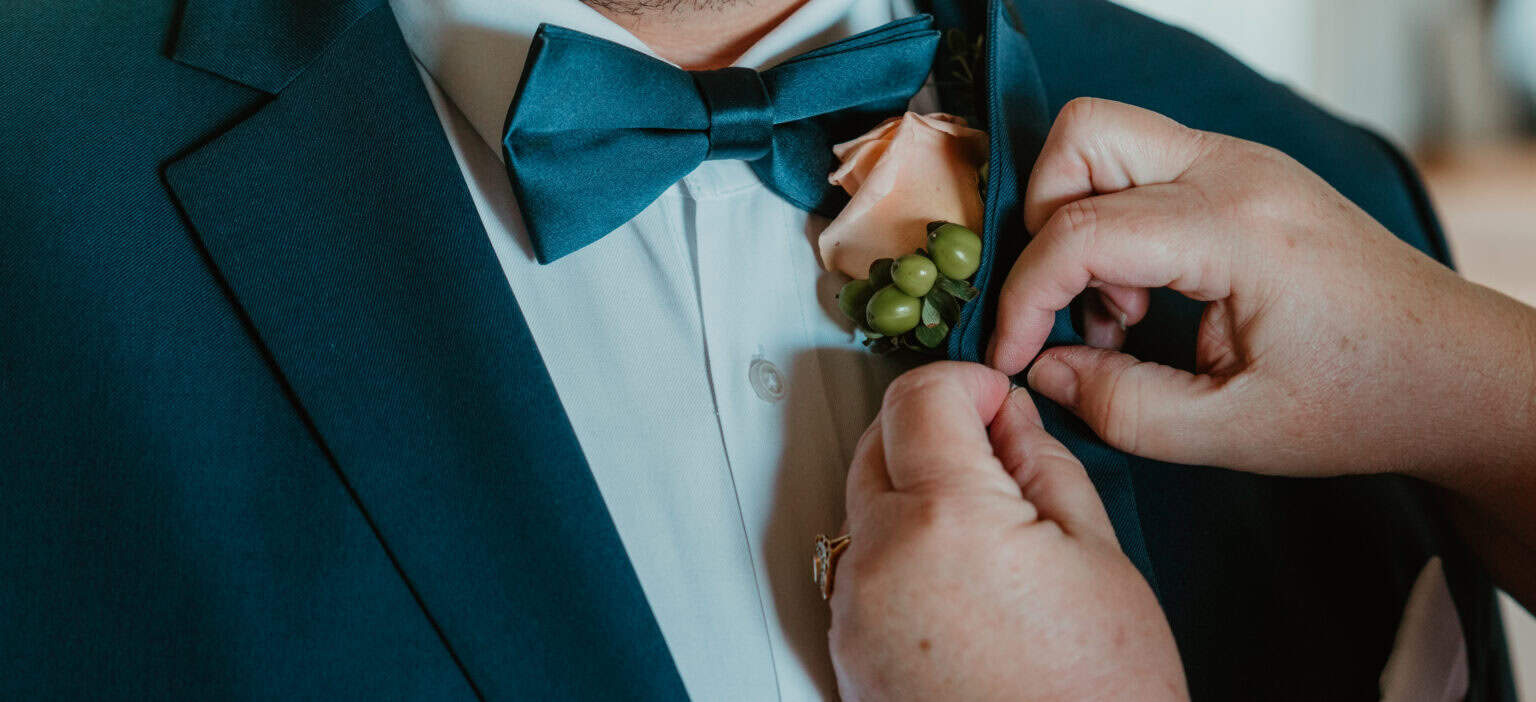 Groom getting ready with peach rose boutonniere pinned on navy suit in Virginia Beach wedding