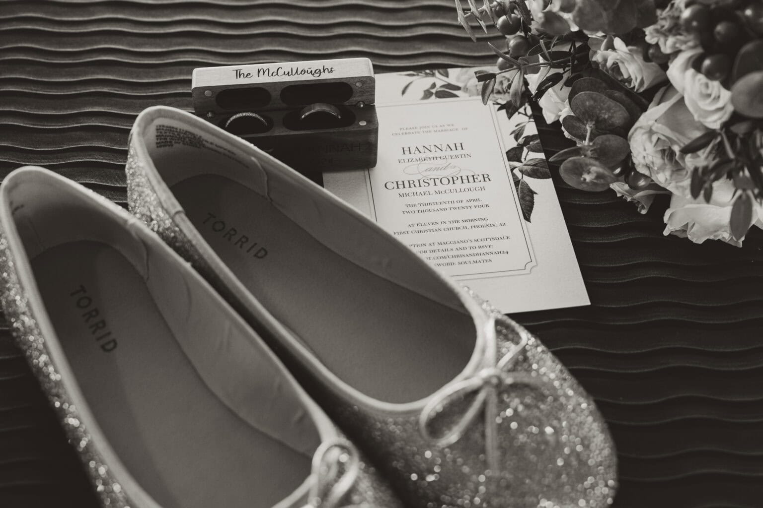 Black and white flat lay with wedding shoes, rings, invitation, and personalized ring box for Virginia Beach couple