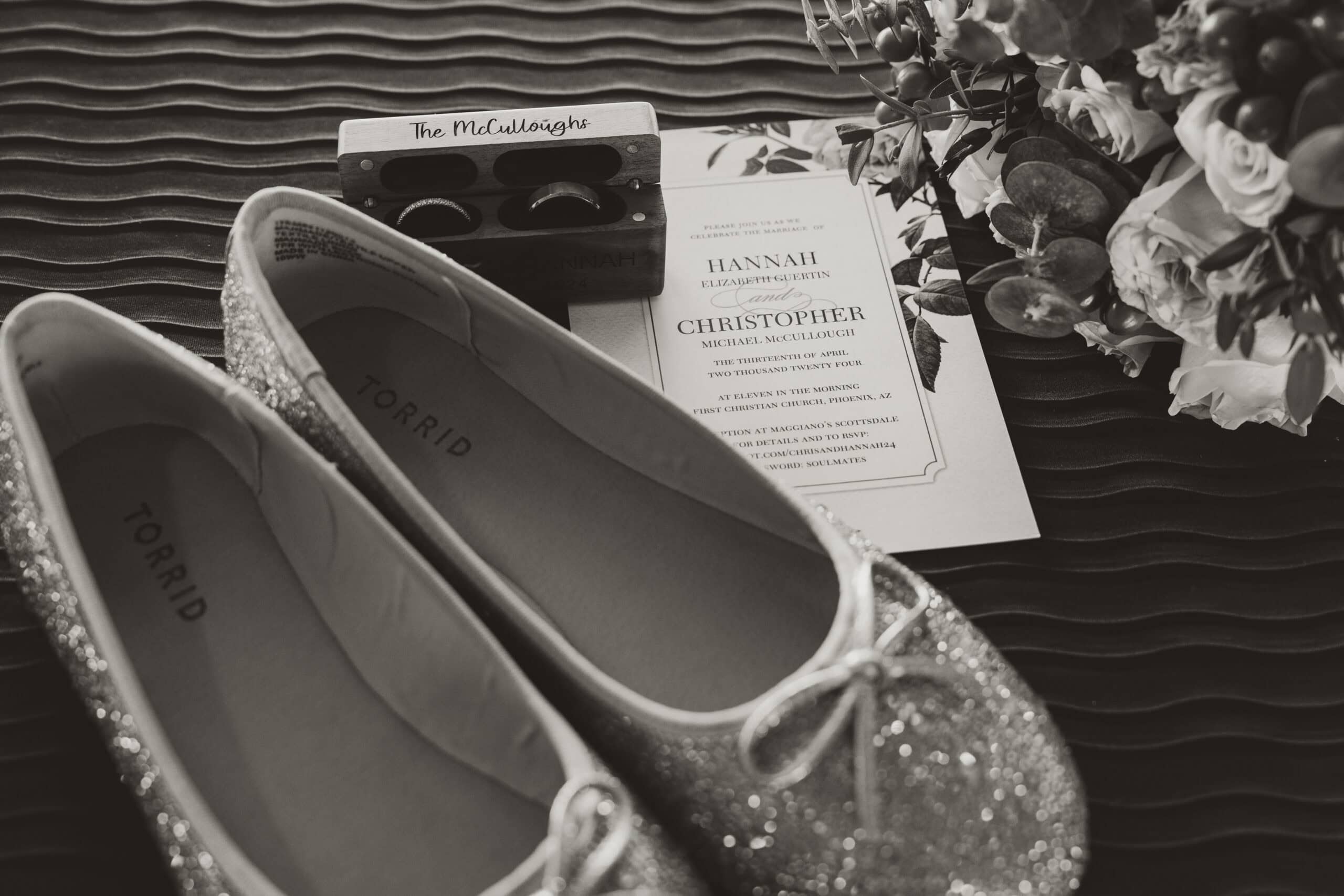 Black and white flat lay with wedding shoes, rings, invitation, and personalized ring box for Virginia Beach couple