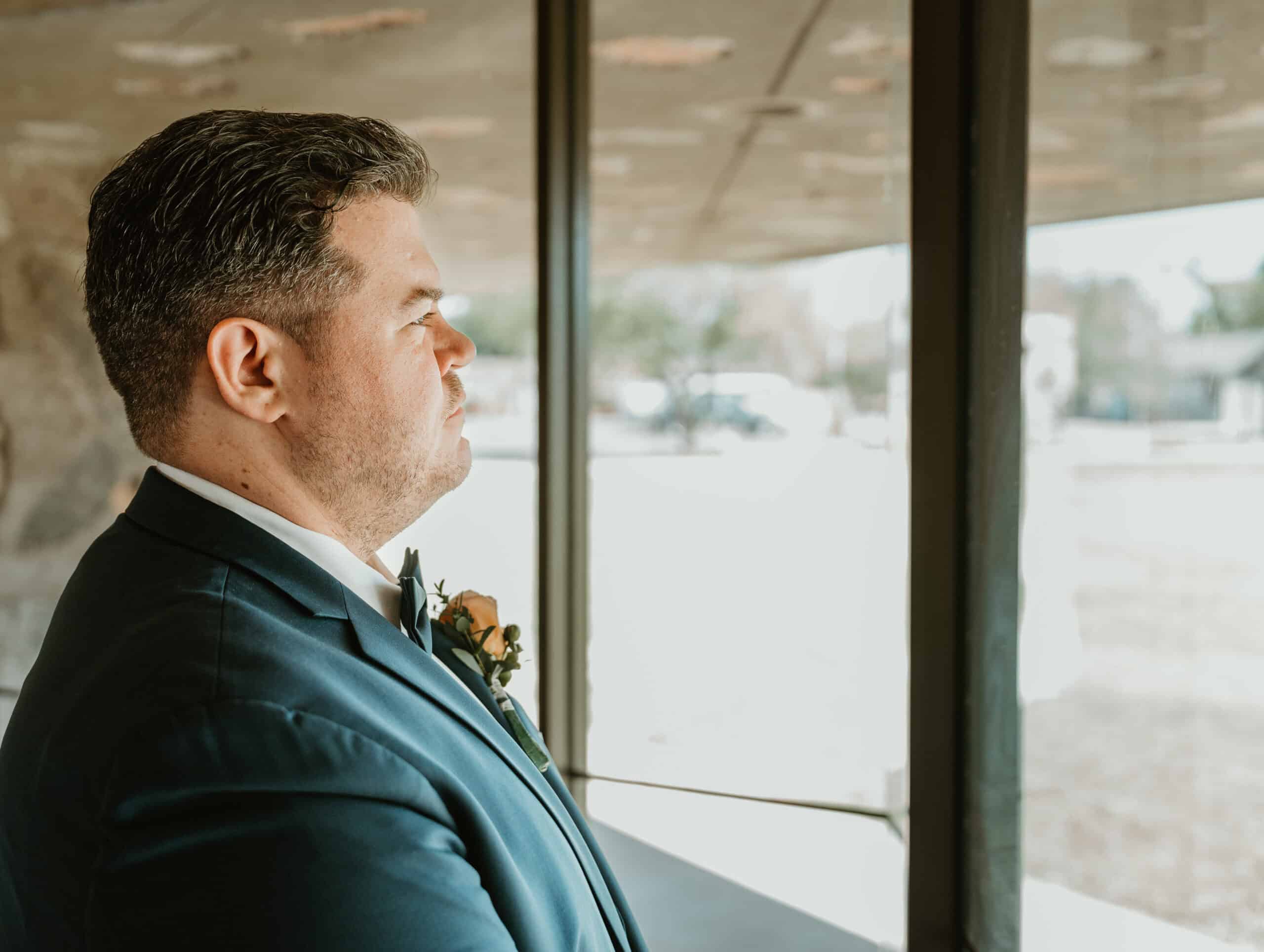 Groom in tuxedo looking out window before ceremony at Virginia Beach wedding venue
