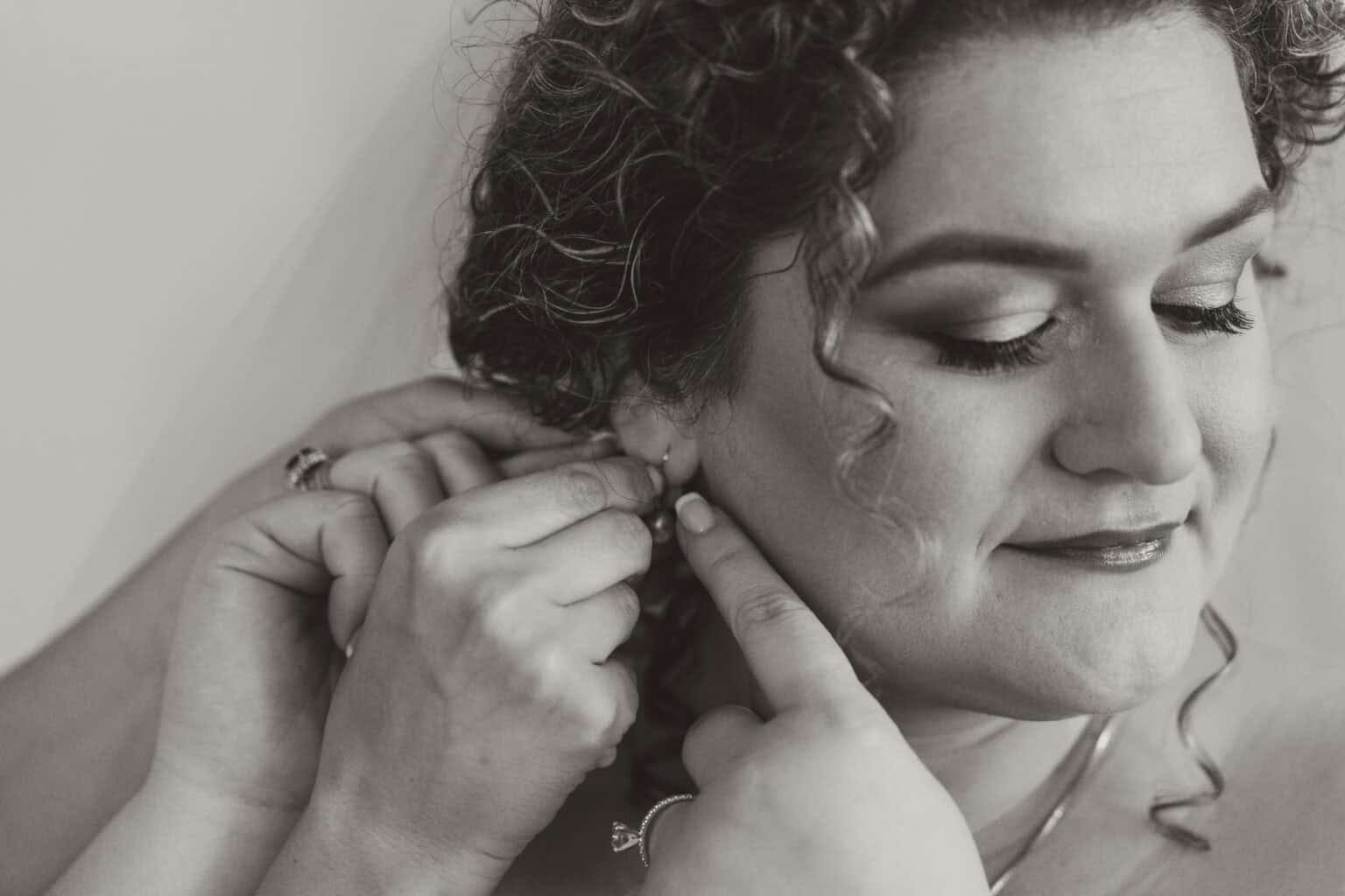 Bride smiling while putting on earrings before wedding ceremony in Virginia Beach
