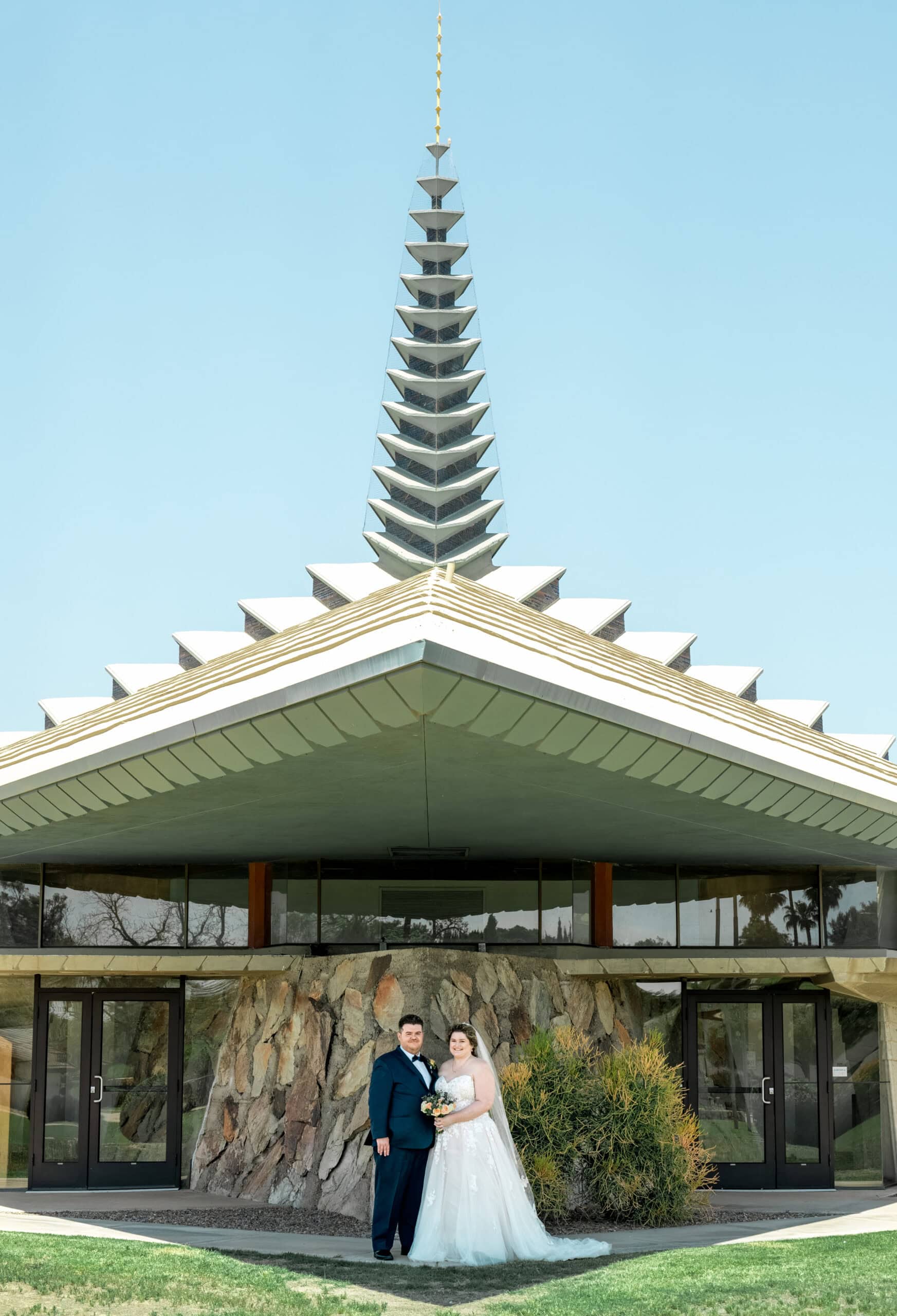 Bride and groom standing outside mid-century modern church with geometric steeple in Virginia Beach wedding portrait