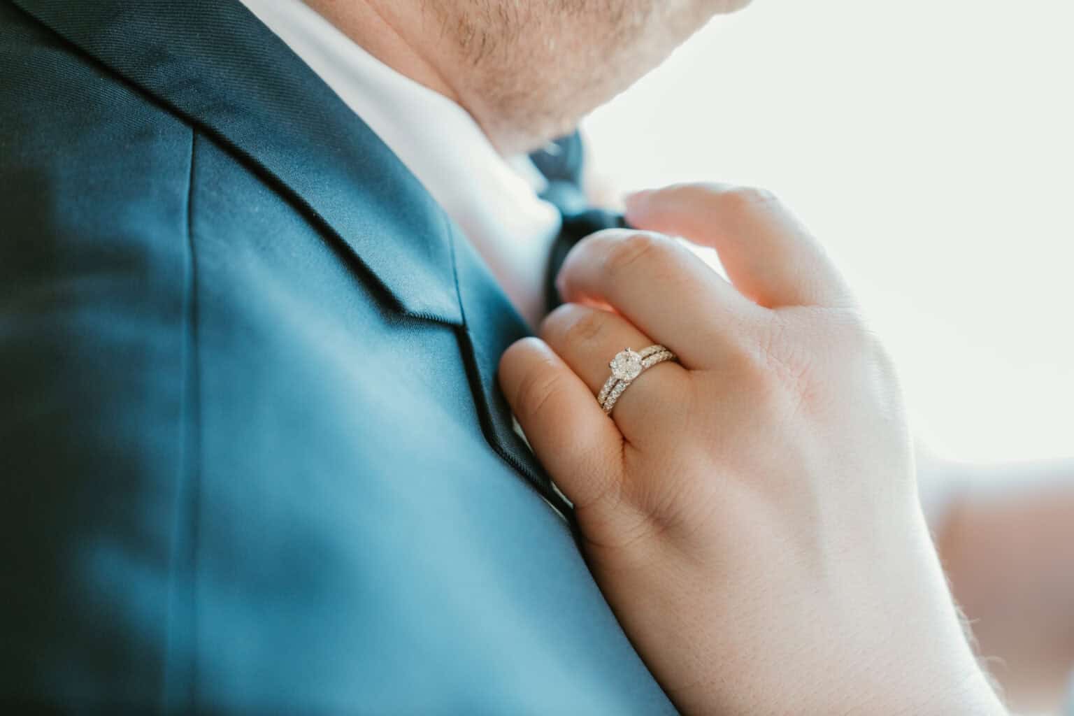 Bride’s hand with diamond ring adjusting groom’s suit during Virginia Beach wedding