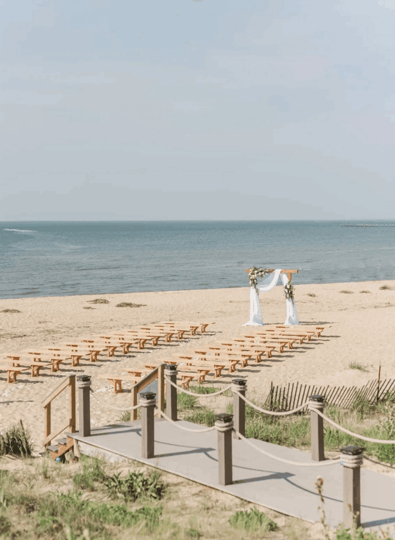 A scenic beach wedding setup with a floral arch and wooden benches on the sand, beautifully framed by a Virginia Beach wedding photographer’s lens.