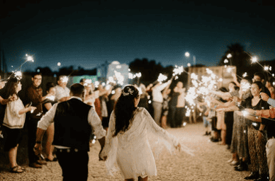 Bride and groom walk hand in hand through a sparkler tunnel surrounded by cheering wedding guests at night in Virginia Beach