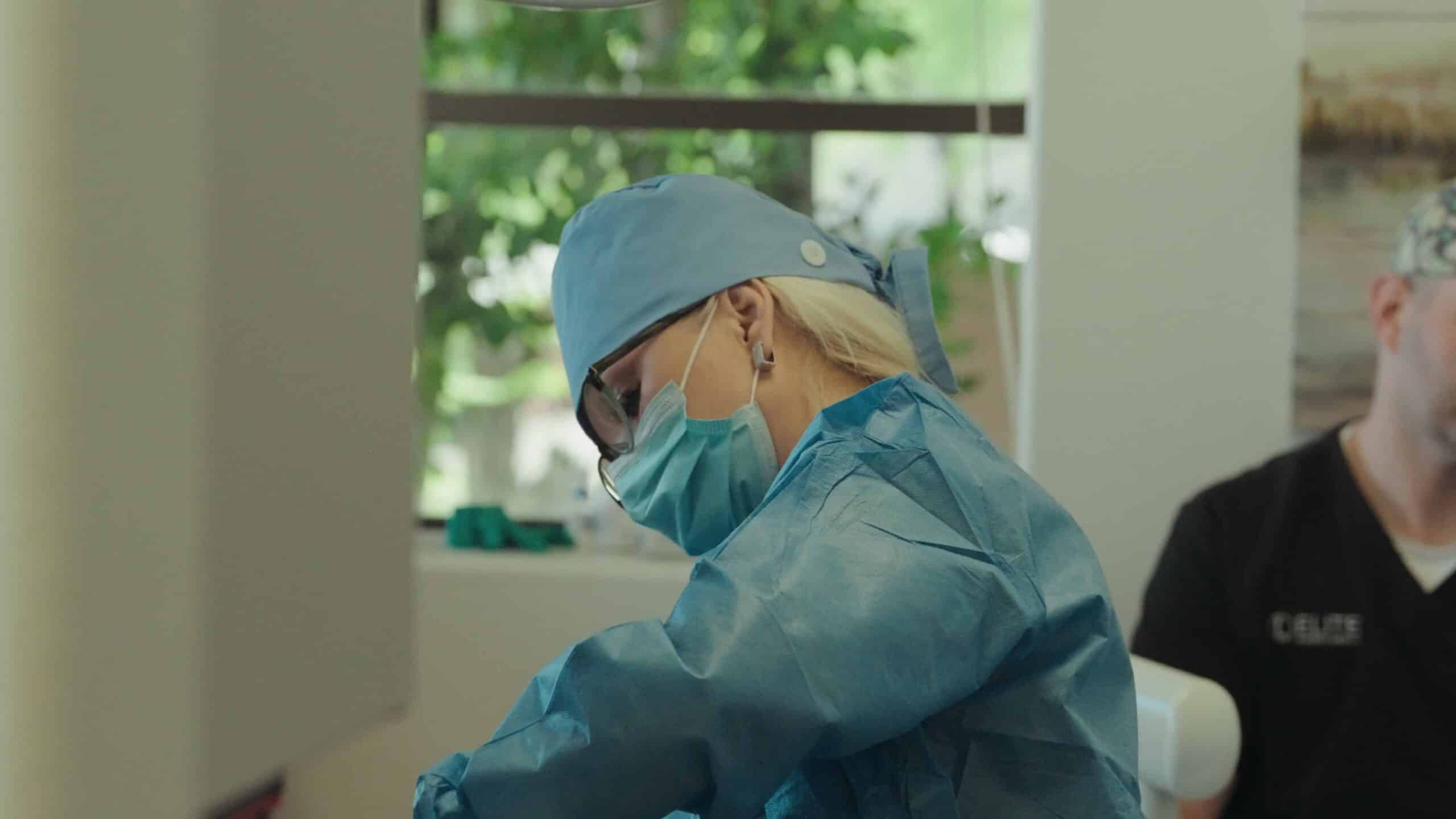 Female healthcare worker wearing surgical scrubs and mask during a medical procedure