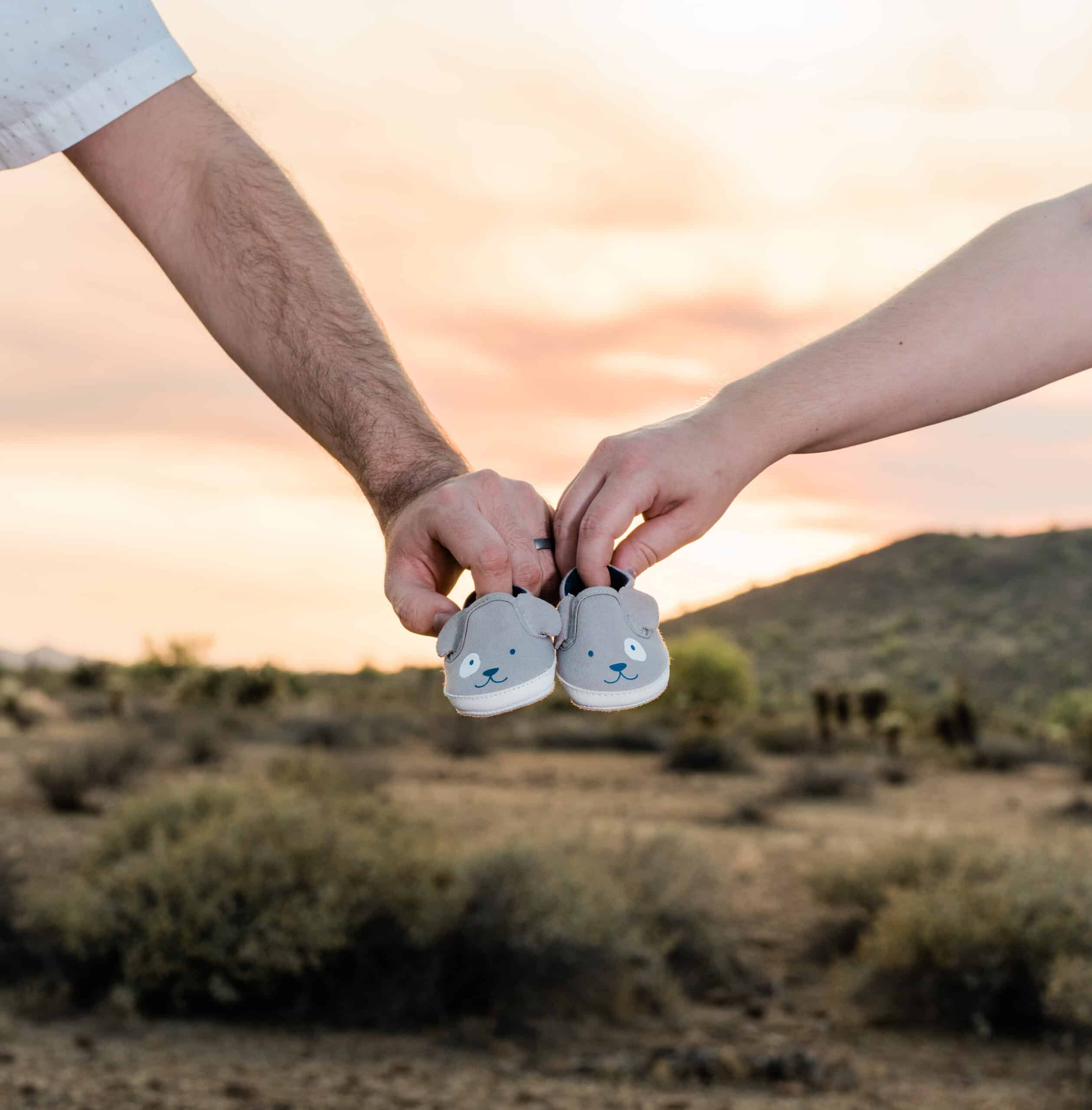 Expecting couple holding tiny puppy-themed baby shoes at sunset, a maternity and pregnancy announcement photo by Captured in VA.