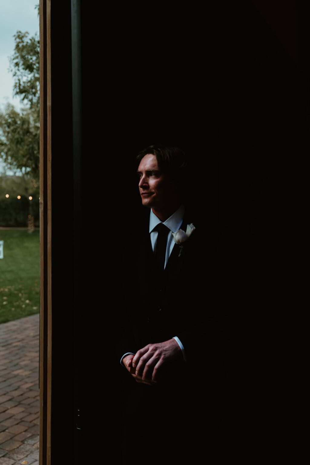 Moody low-light profile portrait of a groom looking out toward the garden before the ceremony, by Captured in VA.