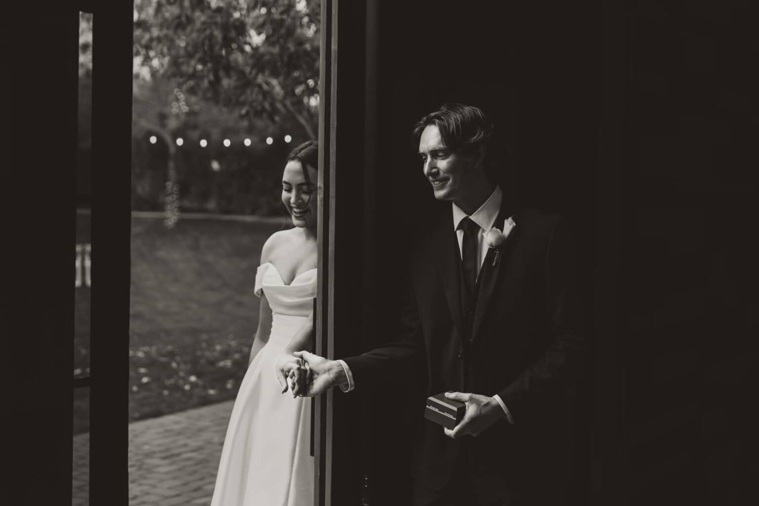 Black and white photo of a bride and groom sharing a private first touch around a corner before the ceremony, the groom holding a ring box, by Captured in VA.
