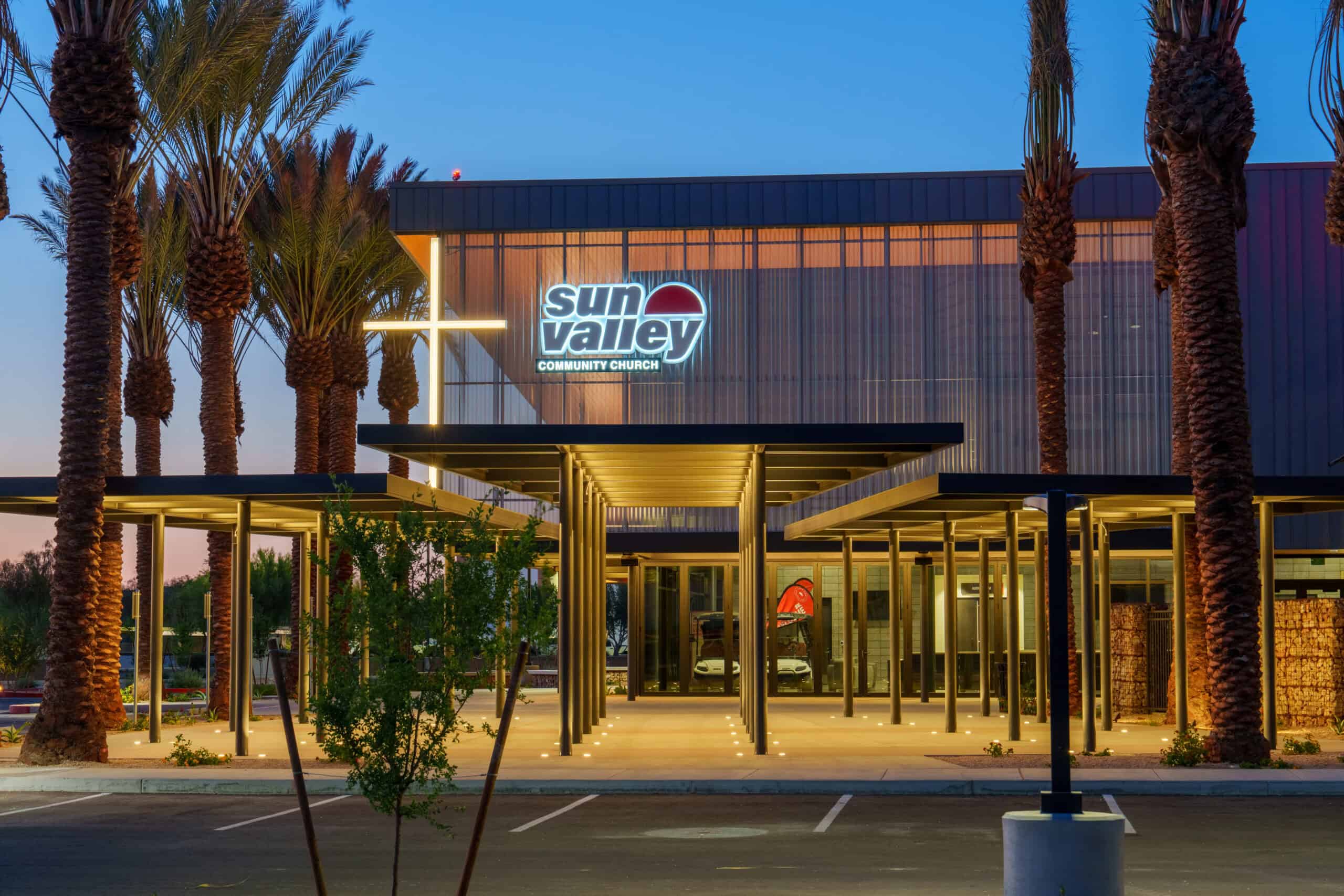 Illuminated main entrance of Sun Valley Community Church at blue hour with palm trees and a lit cross, commercial architectural photography by Captured in VA.