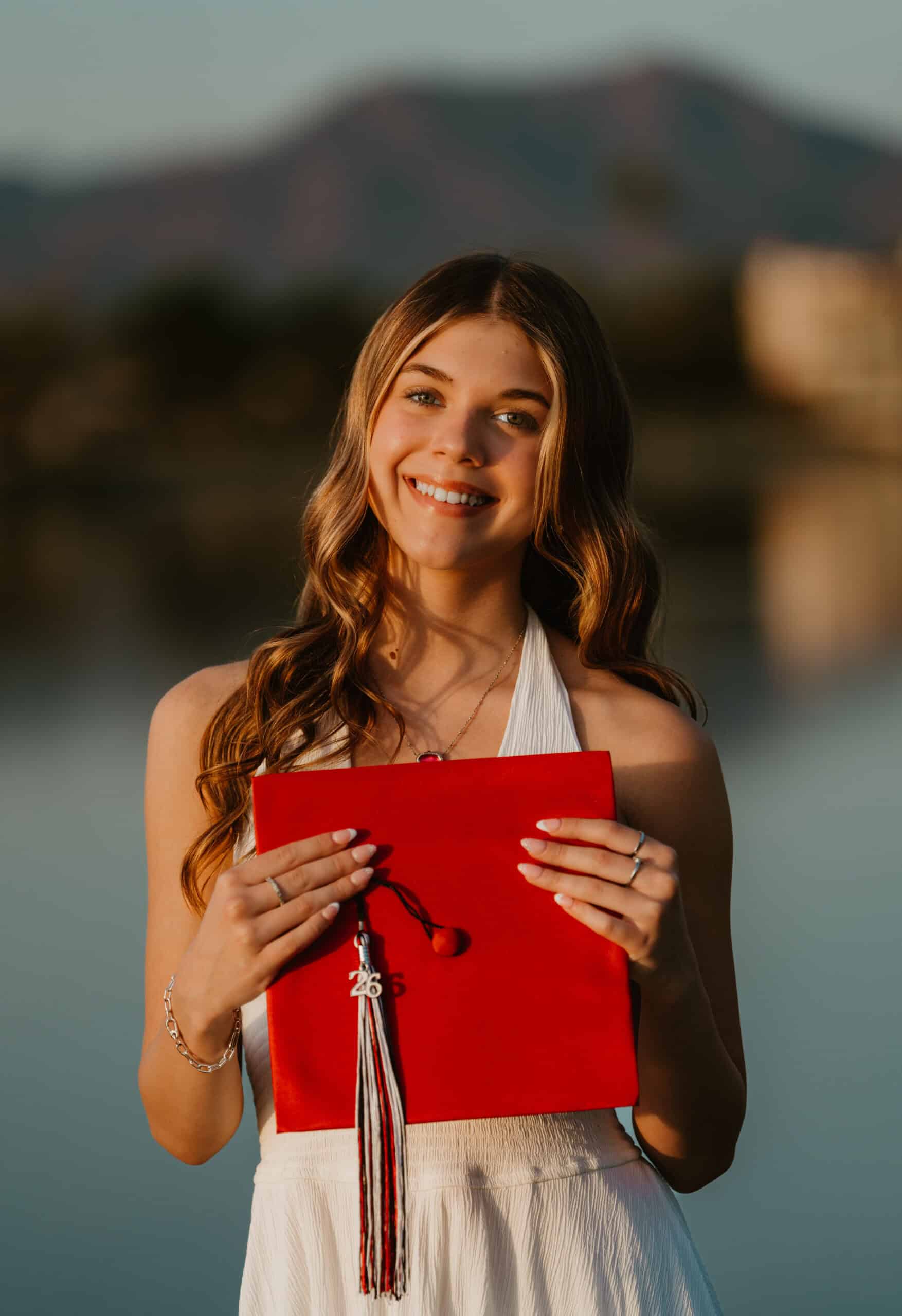 Class of 2026 high school senior holding a red graduation cap with a '26' tassel against a lake-and-mountain backdrop, by Captured in VA.