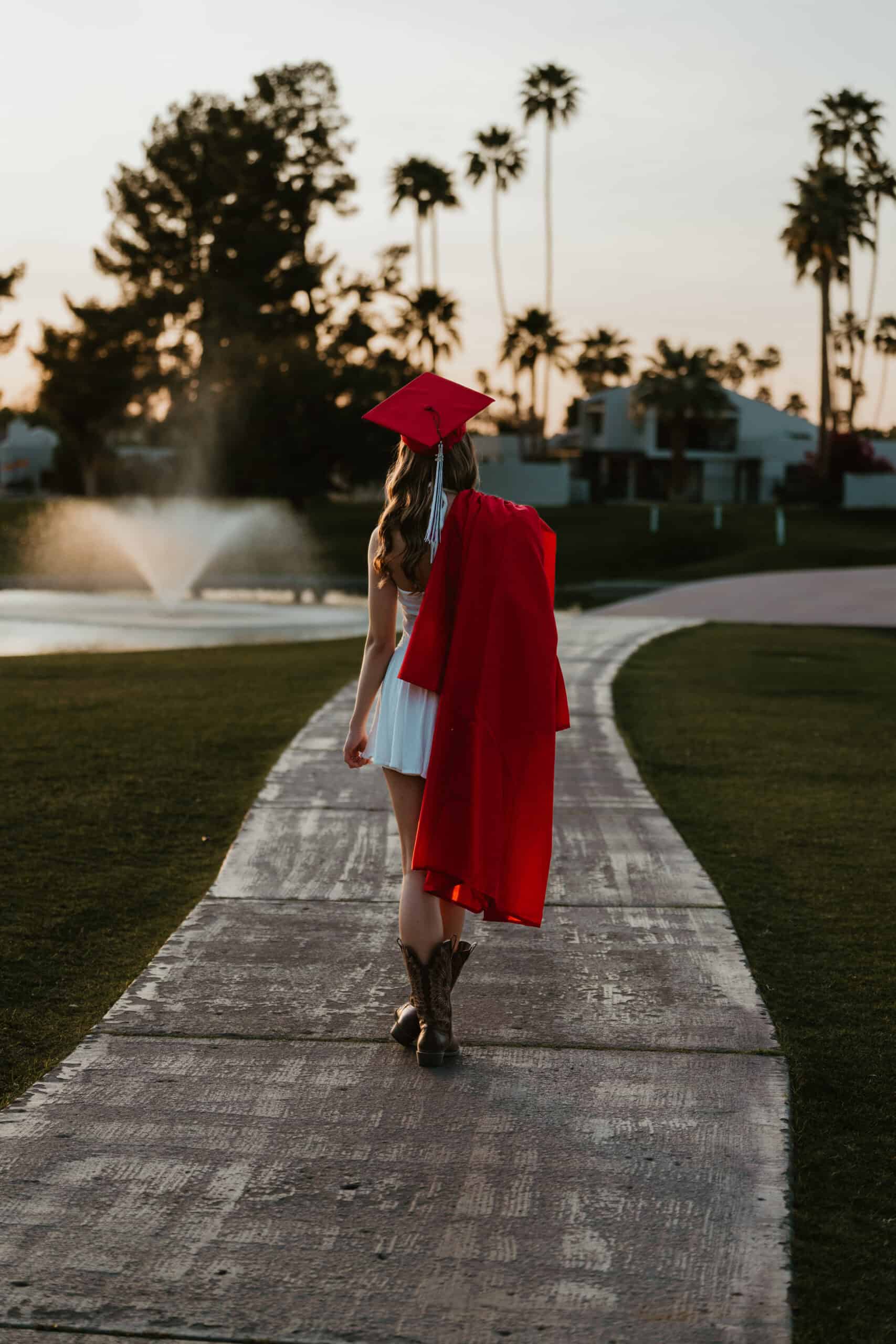 High school senior in a white dress and cowboy boots posing beside a still lake with mountains reflected at dusk, by Captured in VA.