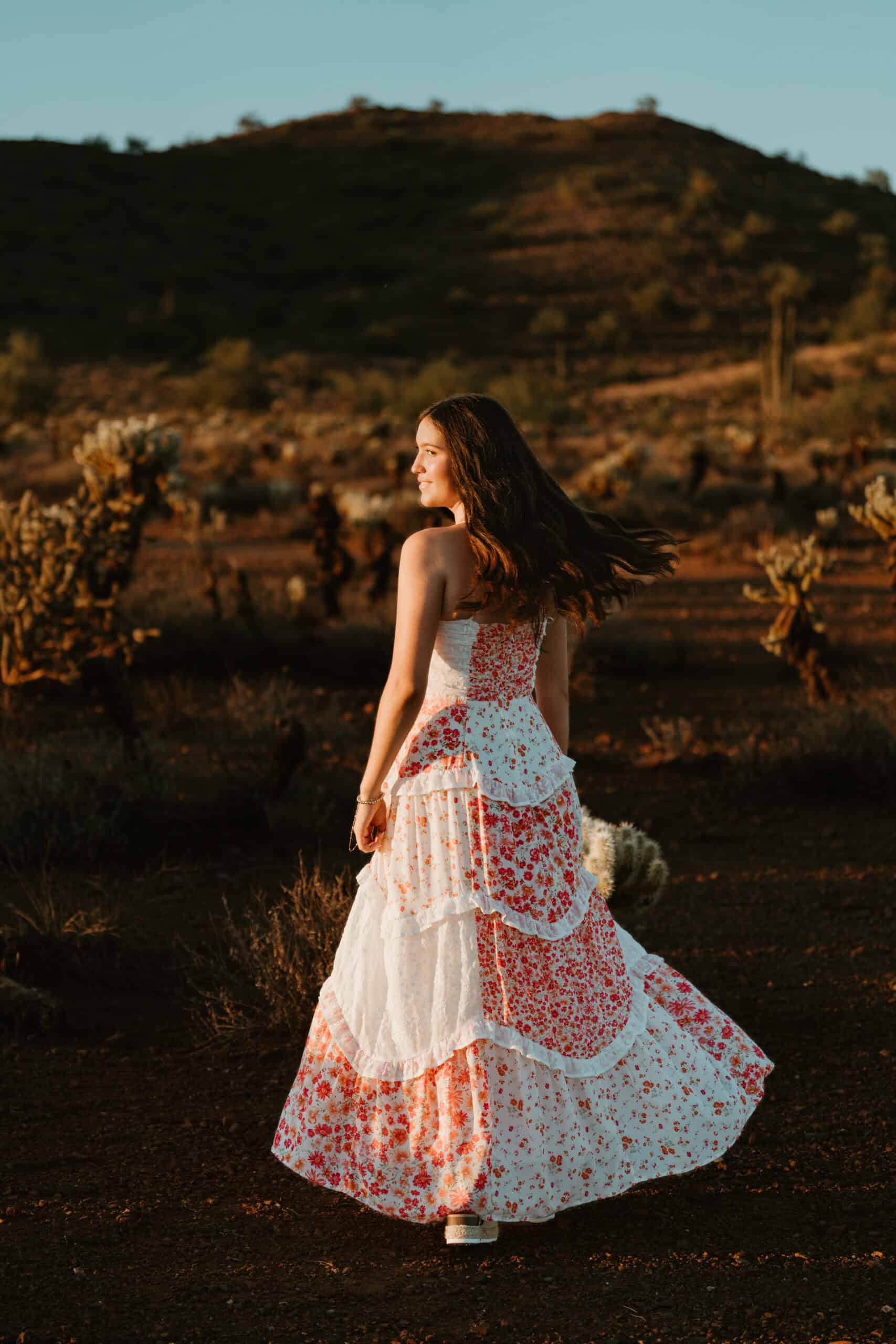 High school senior twirling her floral maxi dress in a desert landscape with cactus and hills at golden hour, by Captured in VA.