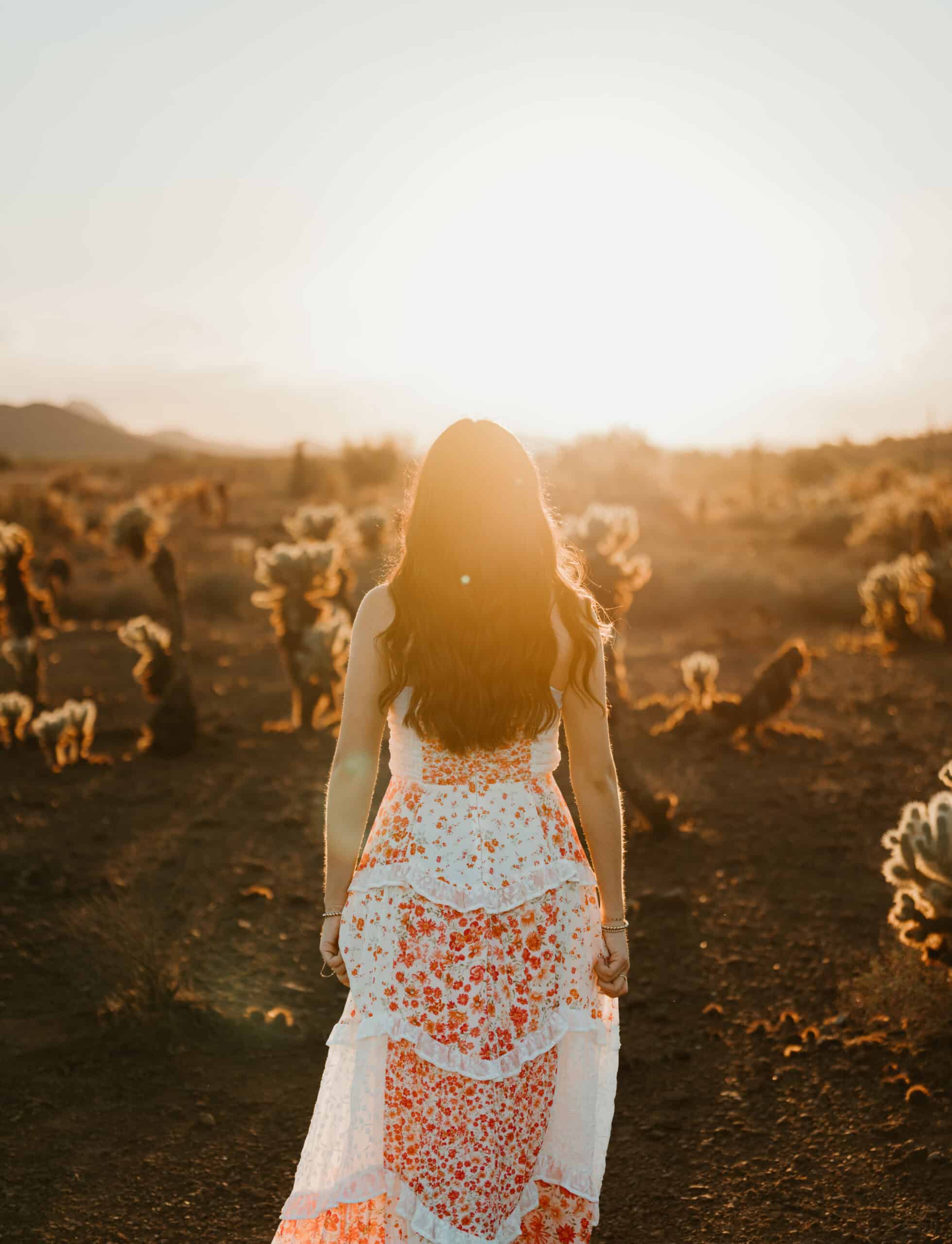 High school senior in a floral maxi dress walking toward the sunset through a desert cactus field, backlit at golden hour, by Captured in VA.