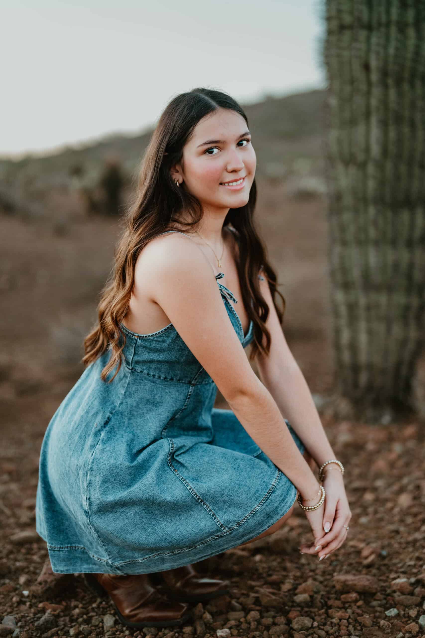 High school senior in a denim dress and cowboy boots glancing over her shoulder in the desert at sunset, by Captured in VA.