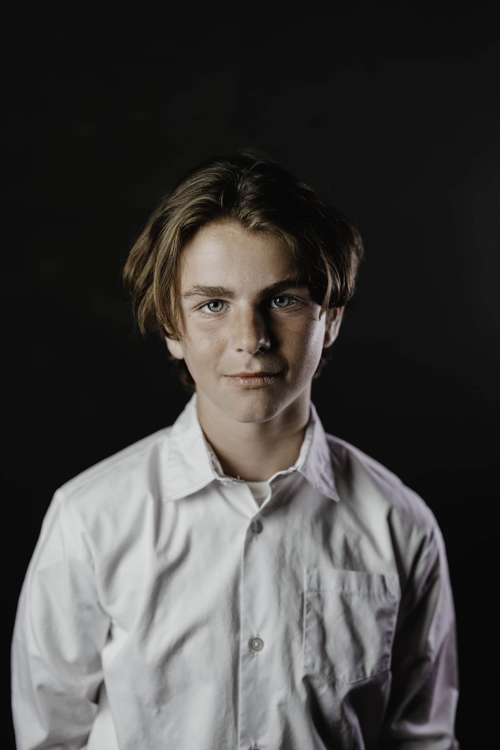 Children's theater headshot of a young actor with tousled hair in a white button-down shirt on a black backdrop, by Captured in VA.