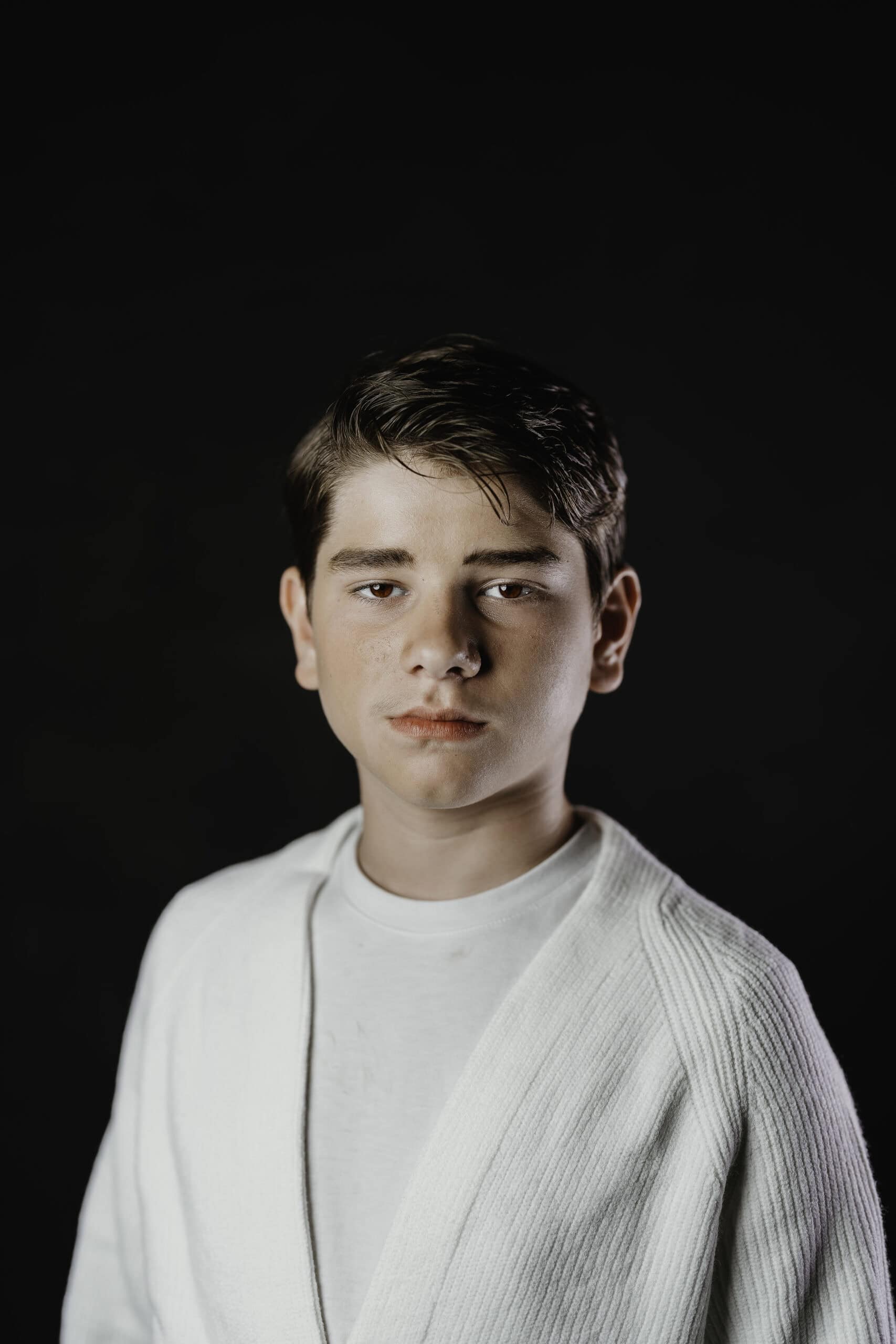 Children's theater headshot of a young actor in a cream cardigan against a black studio backdrop, by Captured in VA.