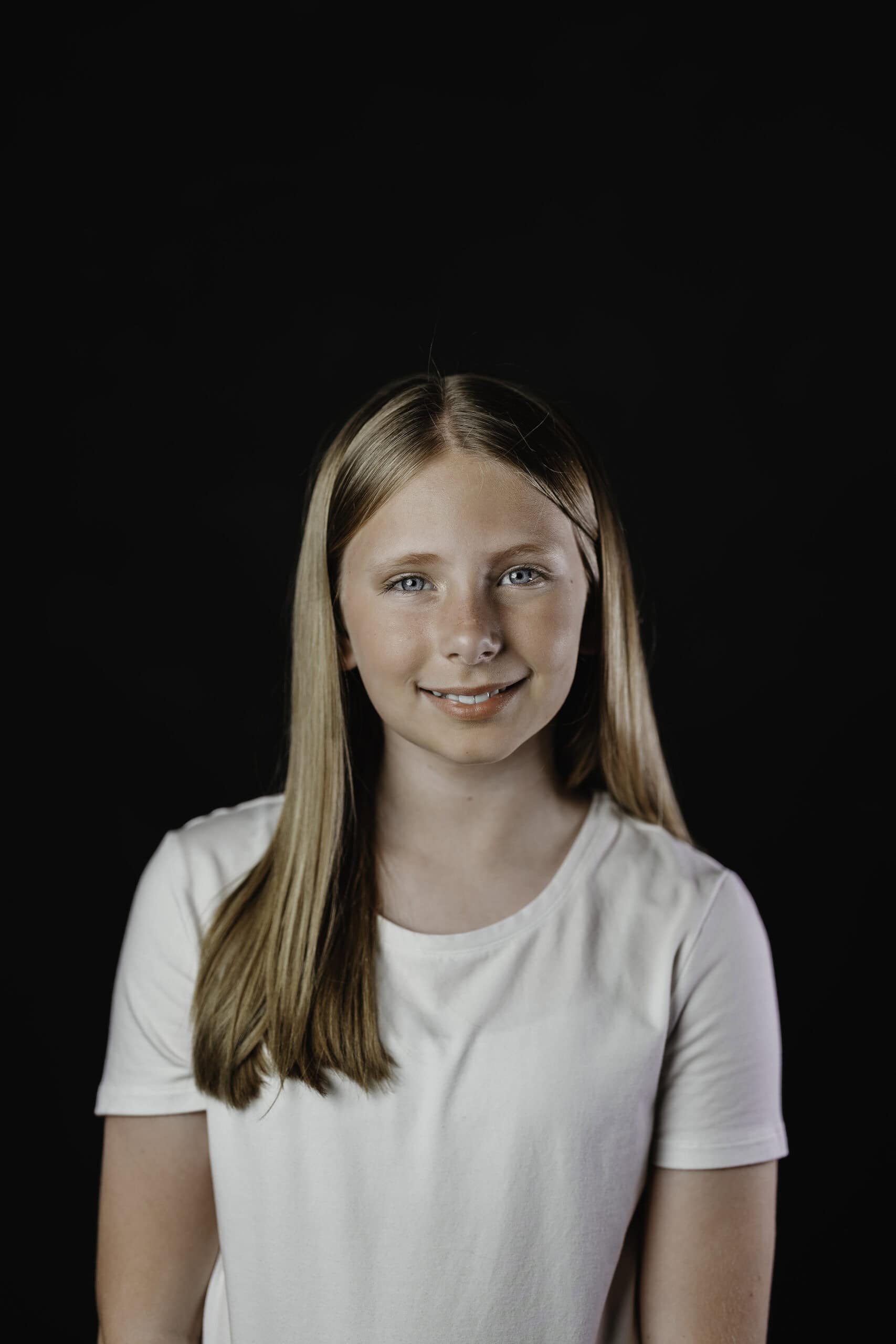 Children's theater headshot of a smiling young actress in a white t-shirt against a black studio backdrop, by Captured in VA.
