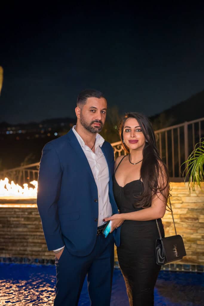 Couple in a blue suit and black dress posing by a fire feature at an outdoor evening birthday party, event photography by Captured in VA.