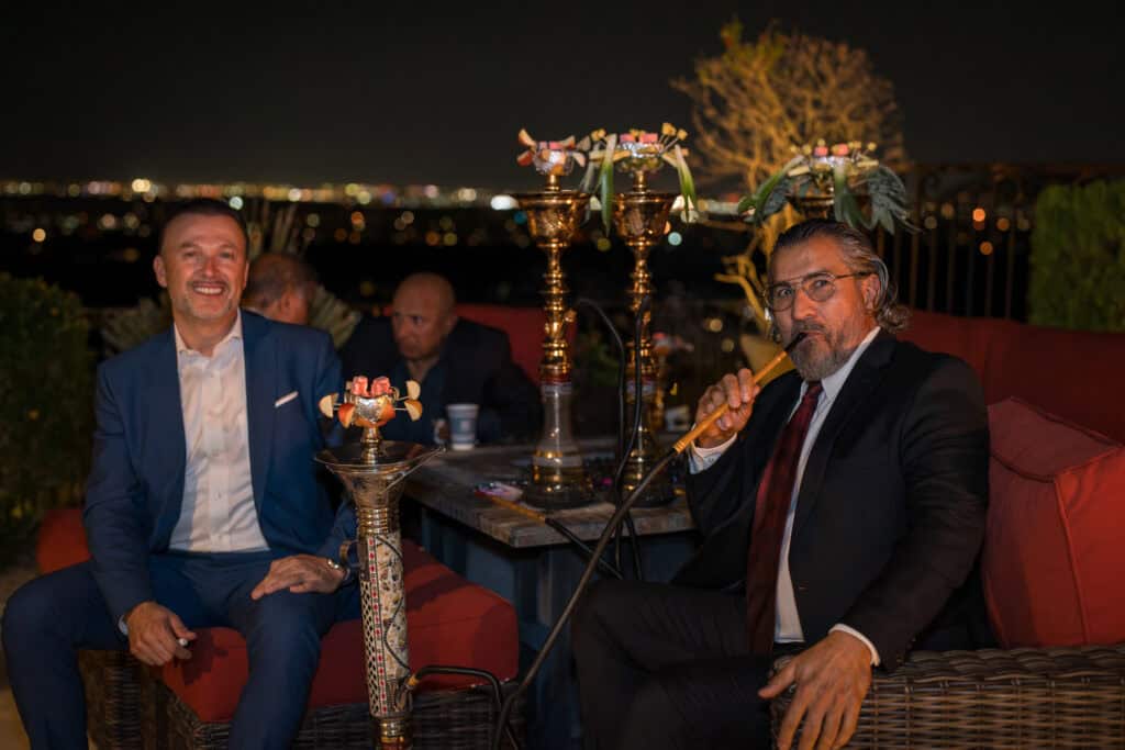 Two well-dressed guests relaxing with hookah on an outdoor patio at a nighttime birthday party, event photography by Captured in VA.