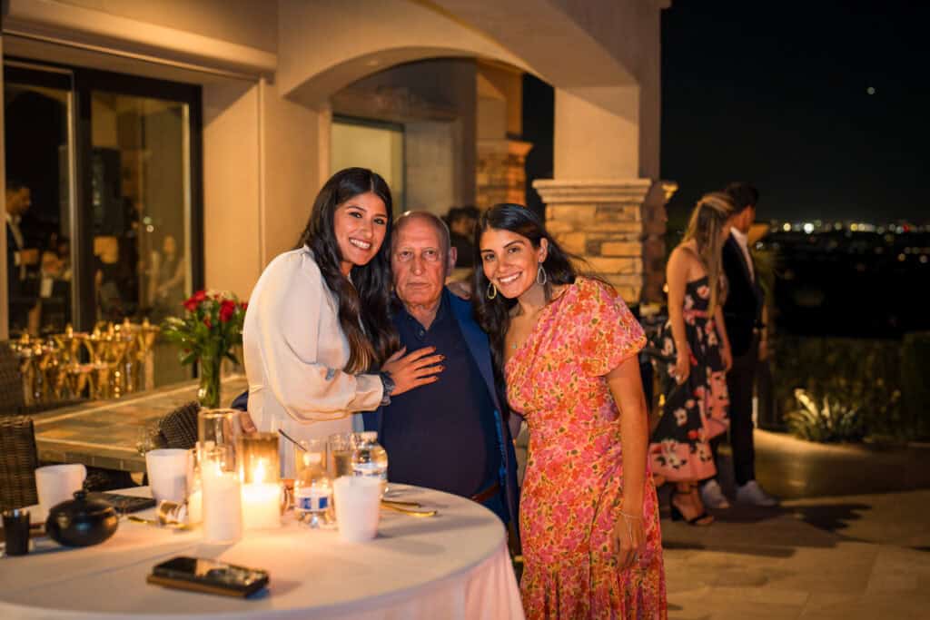 Birthday guest of honor posing with two smiling women at his candlelit outdoor party, event photography by Captured in VA.