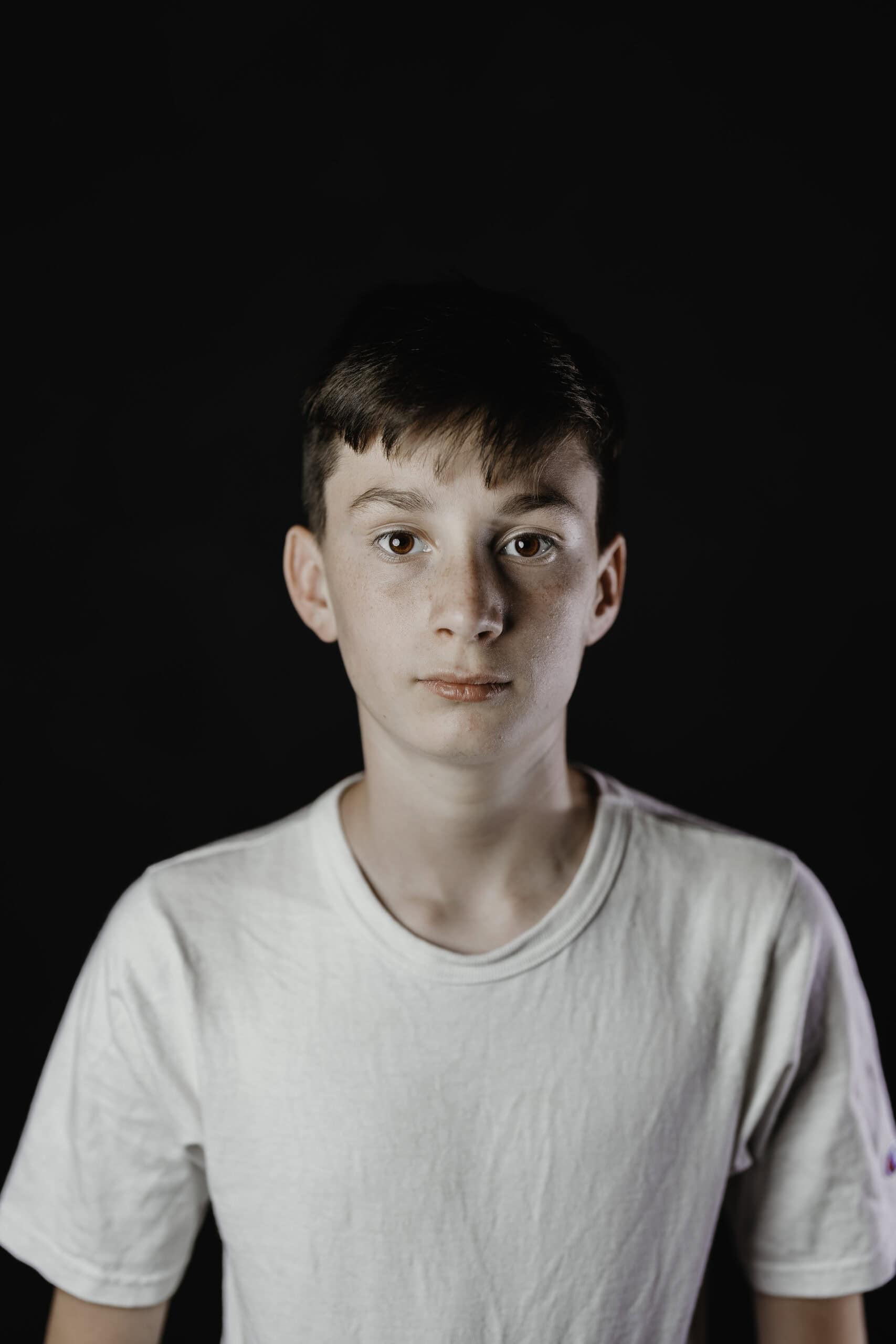 Children's theater headshot of a young actor in a white t-shirt against a black studio backdrop, by Captured in VA.