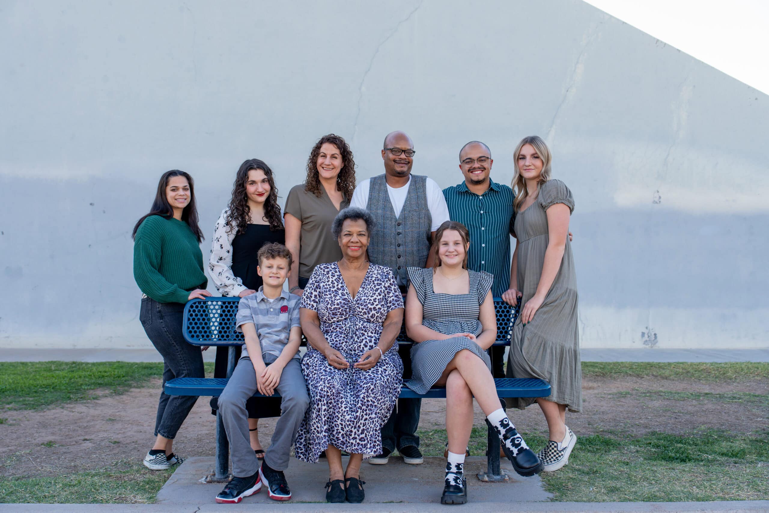 Multigenerational family of nine gathered around a park bench, grandmother seated in the center with kids and grandkids, by Captured in VA.