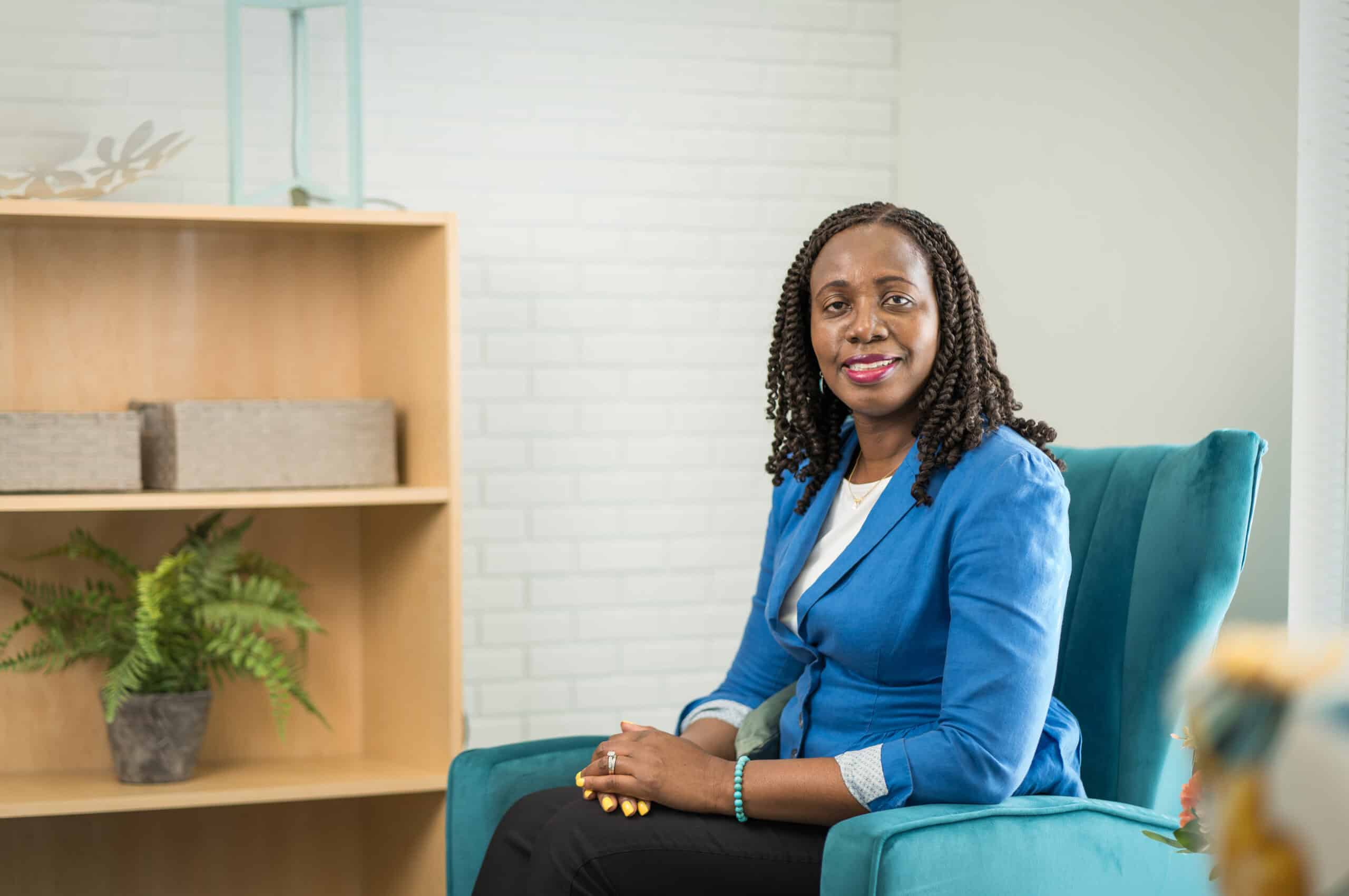 Therapist with locs in a blue blazer seated in a teal armchair in a calm office setting, a professional branding portrait by Captured in VA.