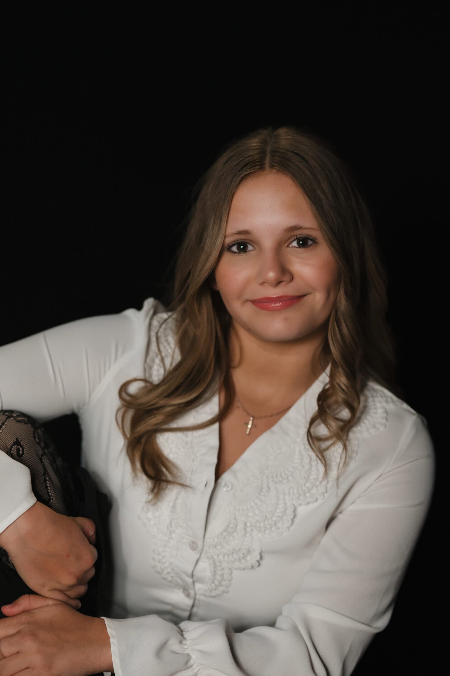 Studio portrait of a smiling girl with wavy hair in a white lace-trimmed blouse against a dark backdrop, by Captured in VA.